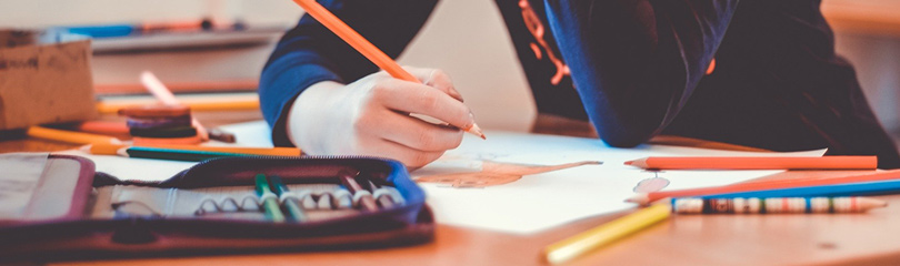 Kind mit Stift in der Hand malt auf Papier.