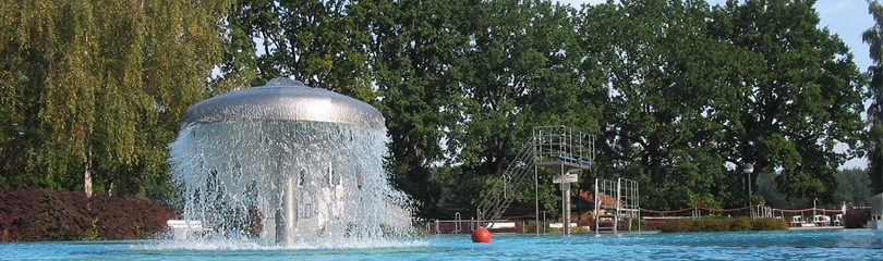Freibad mit Sprungturm im Hintergrund im Vordergrund ein Wasserspiel.